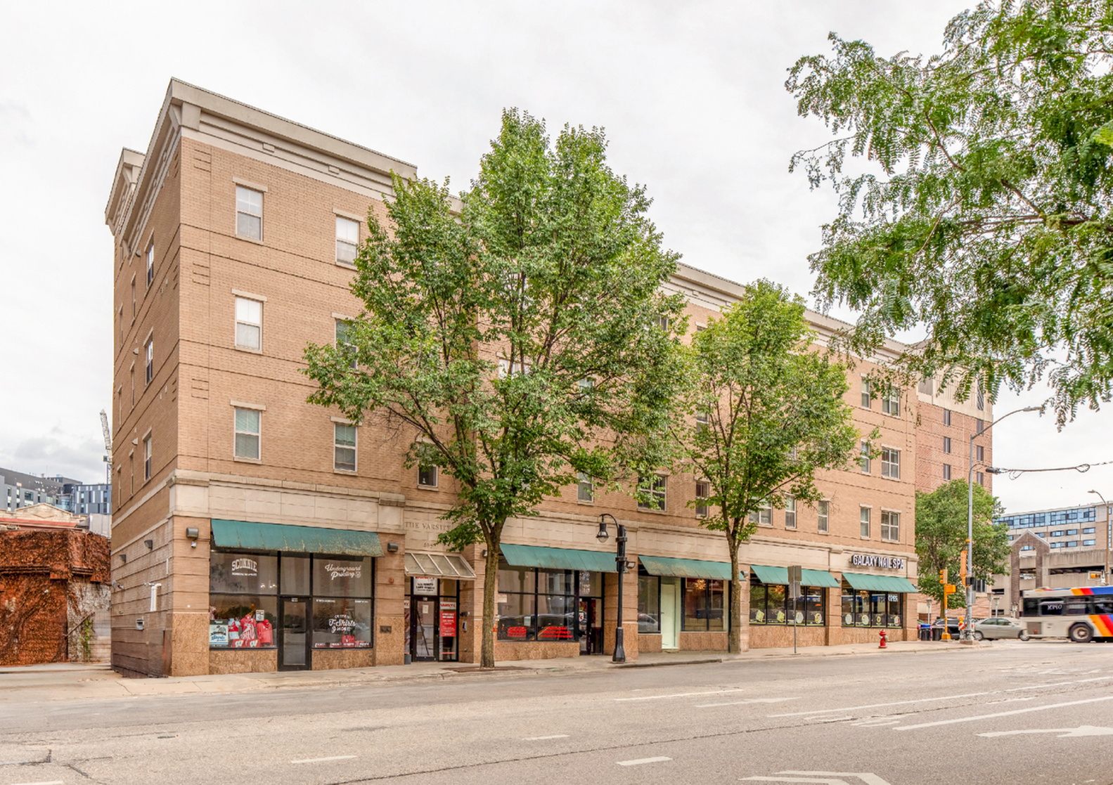 Charming brick apartment building with street-level shops, nestled amongst lush trees.