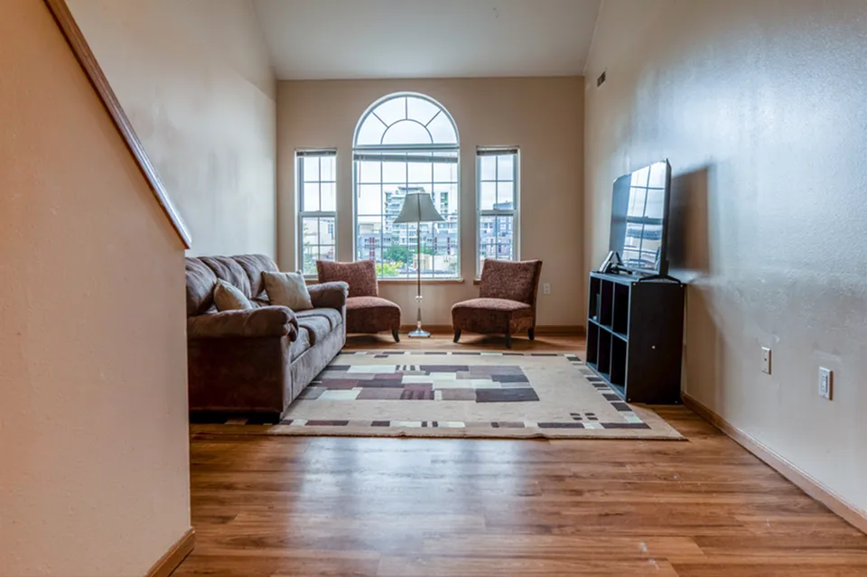 Bright living room with large arched window, comfortable seating, and modern TV setup, offering a welcoming ambiance.