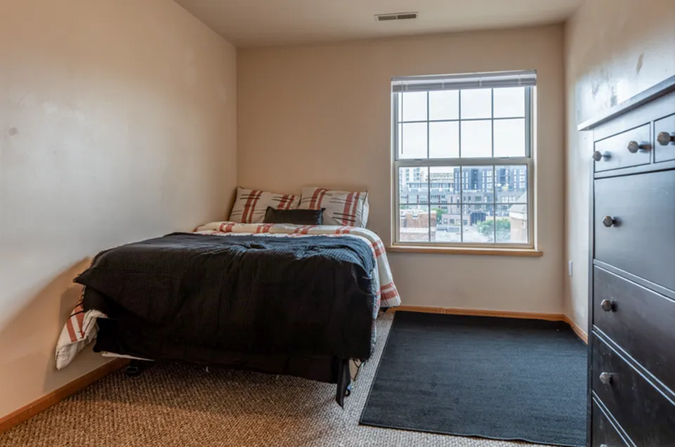 Cozy bedroom with plush bedding and city view, featuring natural light and modern furnishings.
