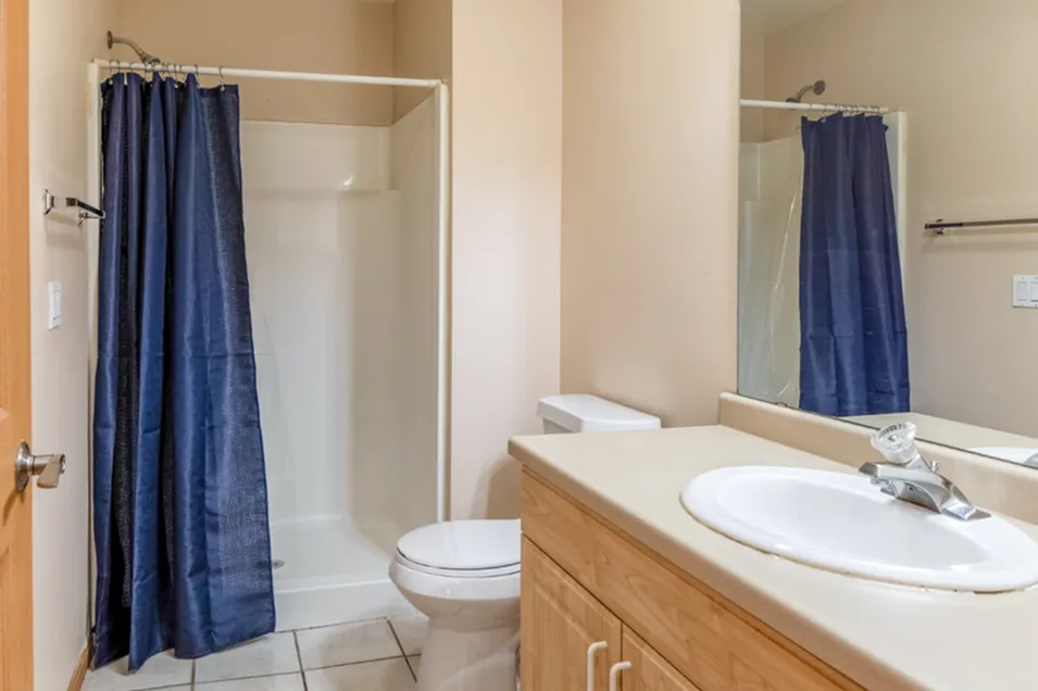 Bright and modern bathroom with a sleek shower, elegant vanity, and deep blue curtain, perfect for comfort and style.