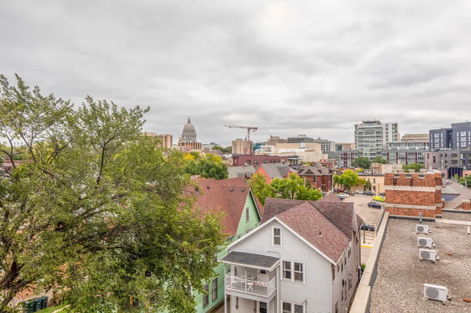 Vibrant cityscape view showcasing charming residential rooftops, lush trees, and iconic architecture under a cloudy sky, highlighting urban living potential.