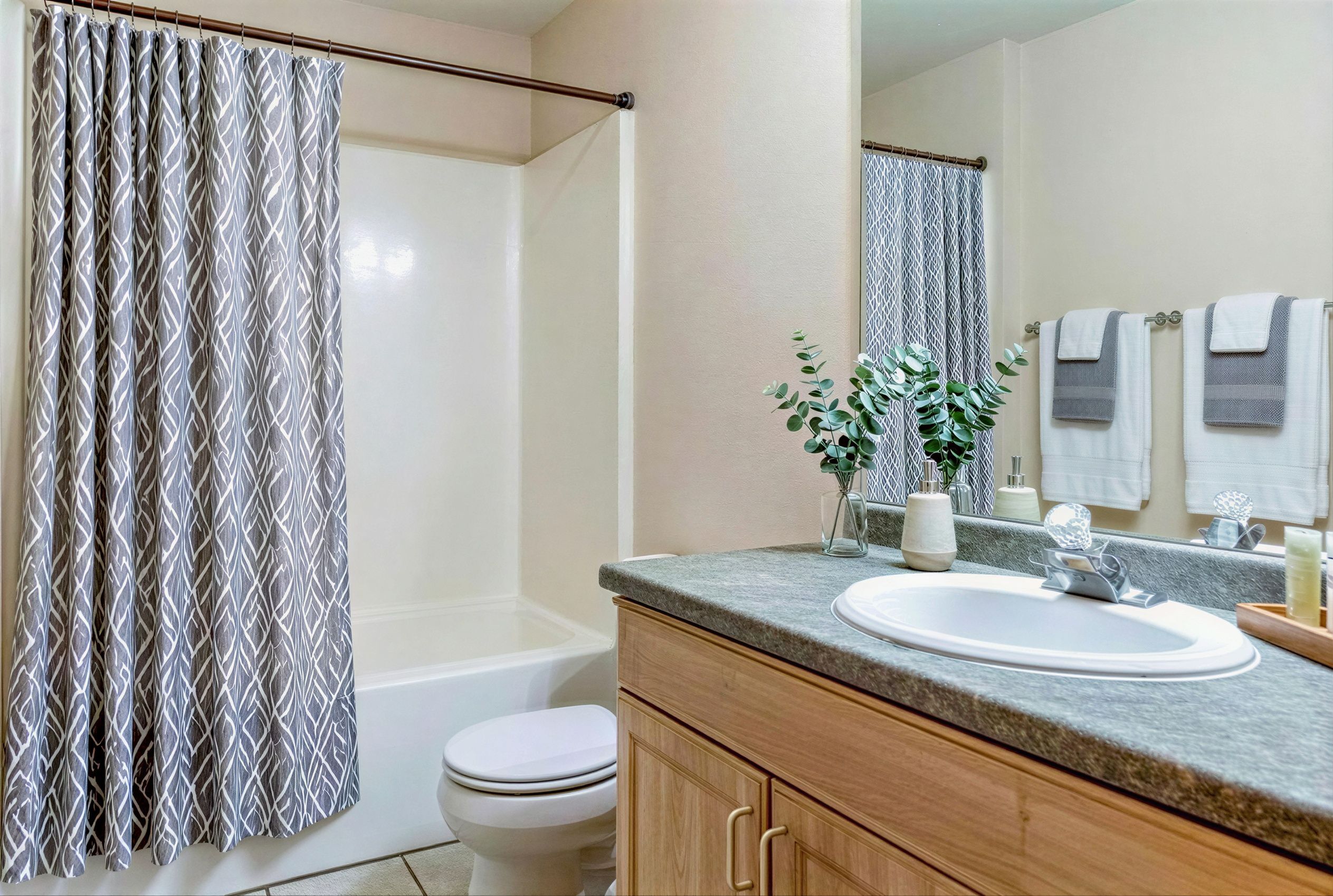 Bright and modern bathroom with elegant white sink, granite countertop, stylish patterned shower curtain, and fresh leafy decor.