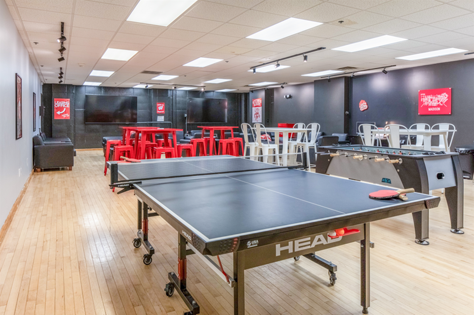 Vibrant recreation room featuring a sleek ping pong table, foosball setup, and modern seating with red accents.