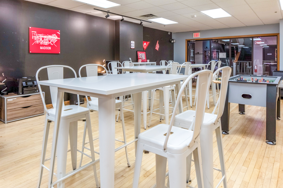 Contemporary recreation room with high-top tables, sleek white chairs, and a foosball table, perfect for lively gatherings.
