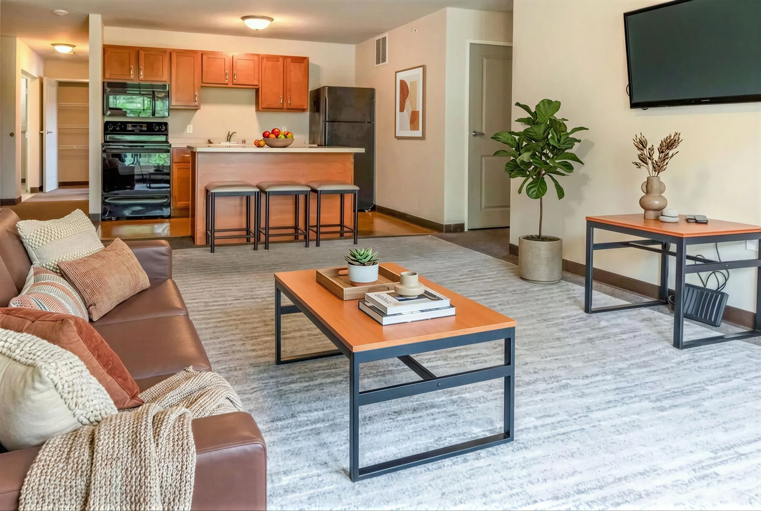 Contemporary living room with elegant decor, cozy seating, and a modern kitchen featuring warm wooden cabinetry and stylish bar stools.