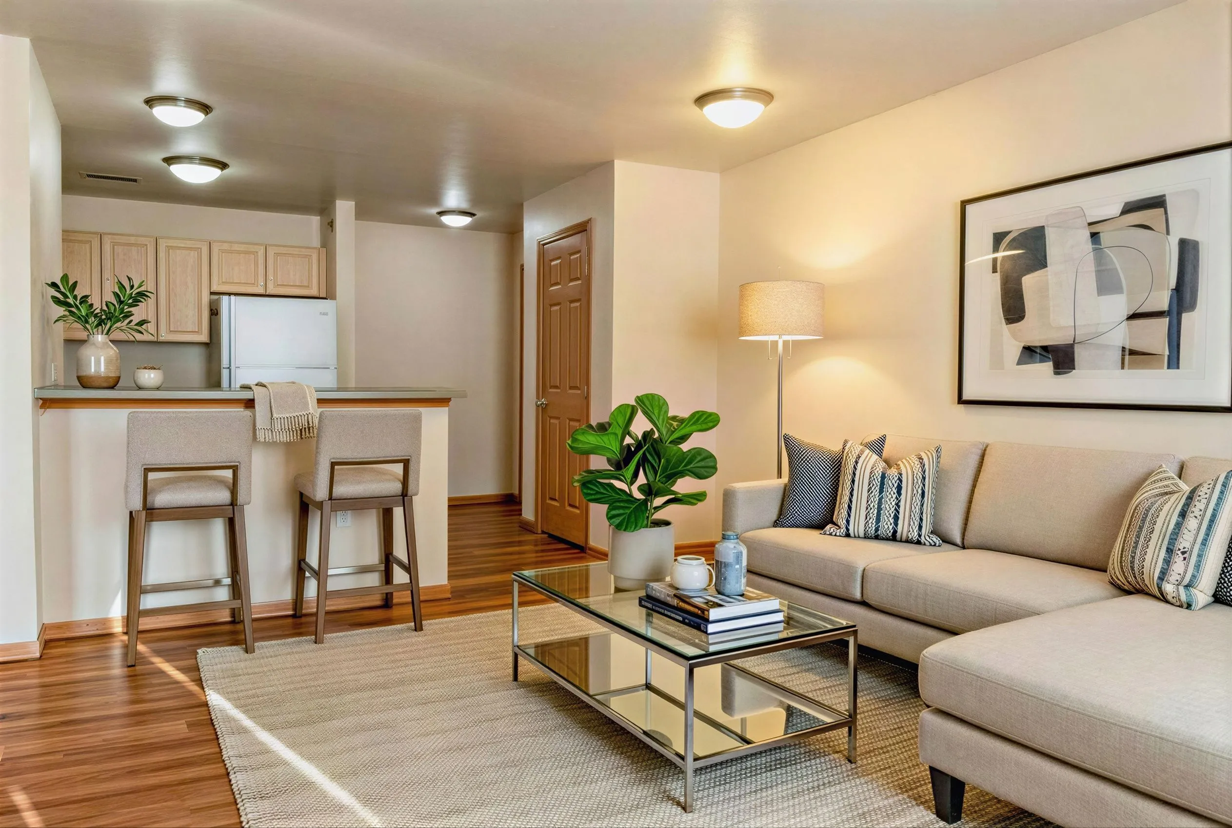 Inviting living space with chic modern decor, featuring a cozy beige sectional, glass coffee table, and a stylish breakfast bar with seating.