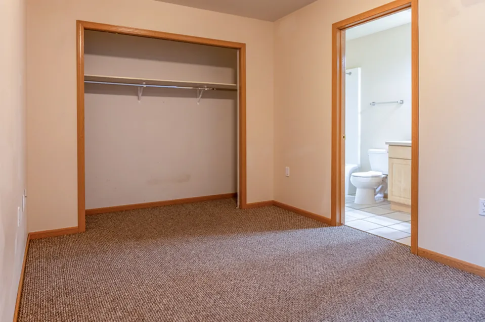 Inviting room with an open closet and cozy carpet, leading to an adjacent bathroom with modern fixtures.