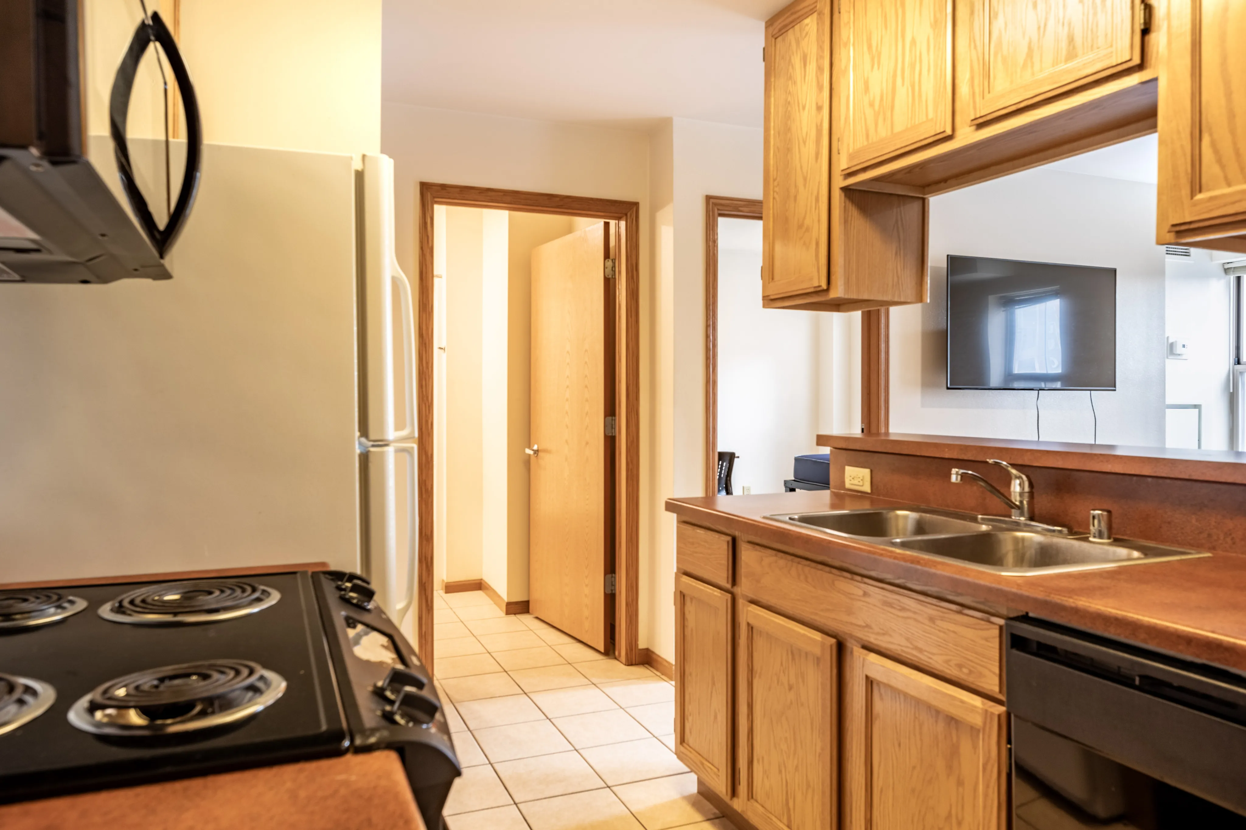Warm kitchen with wooden cabinets, modern appliances, and a view of a cozy living area.