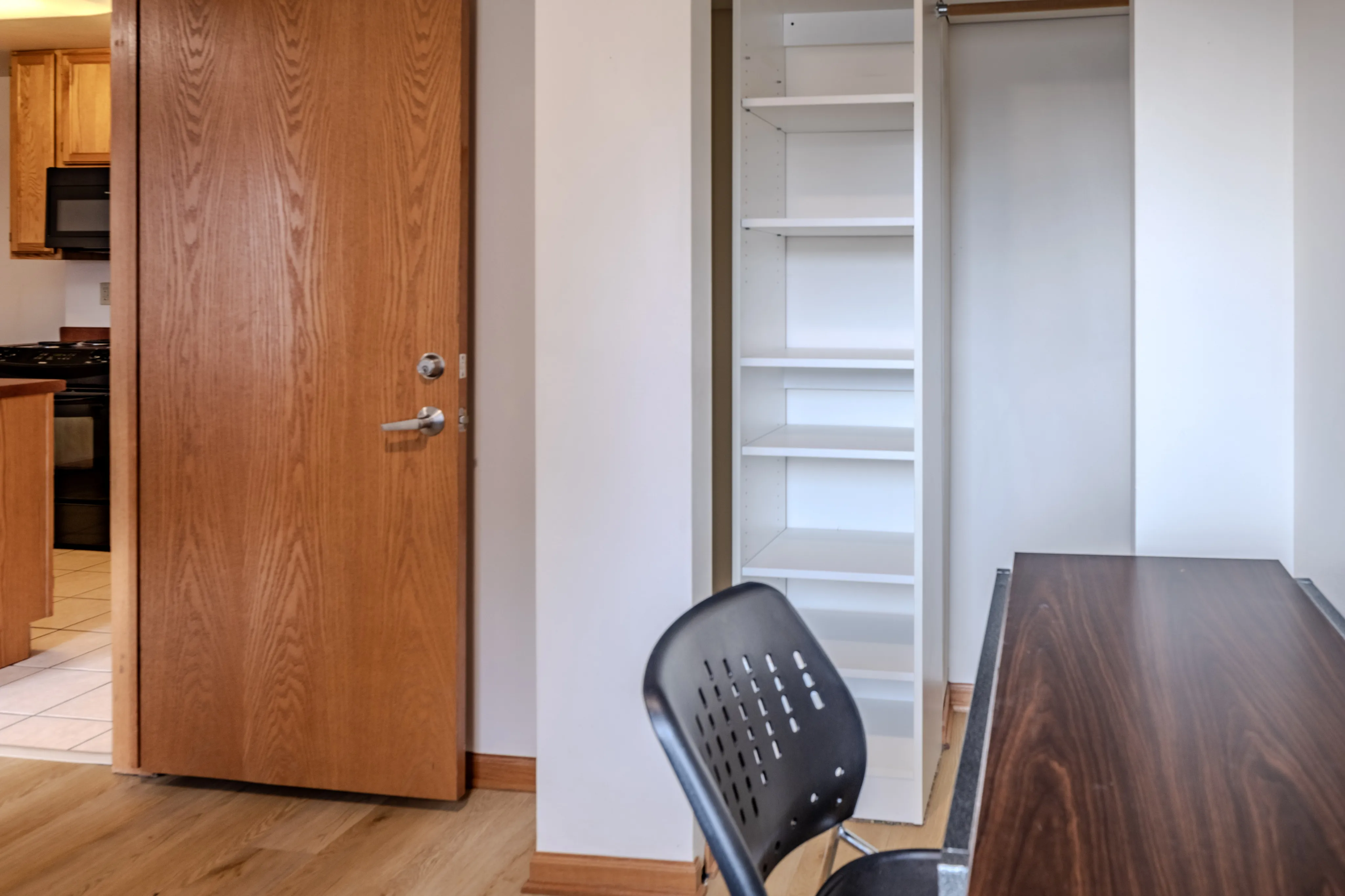 Modern apartment interior showcasing a wooden door, built-in shelving, and partial kitchen view.