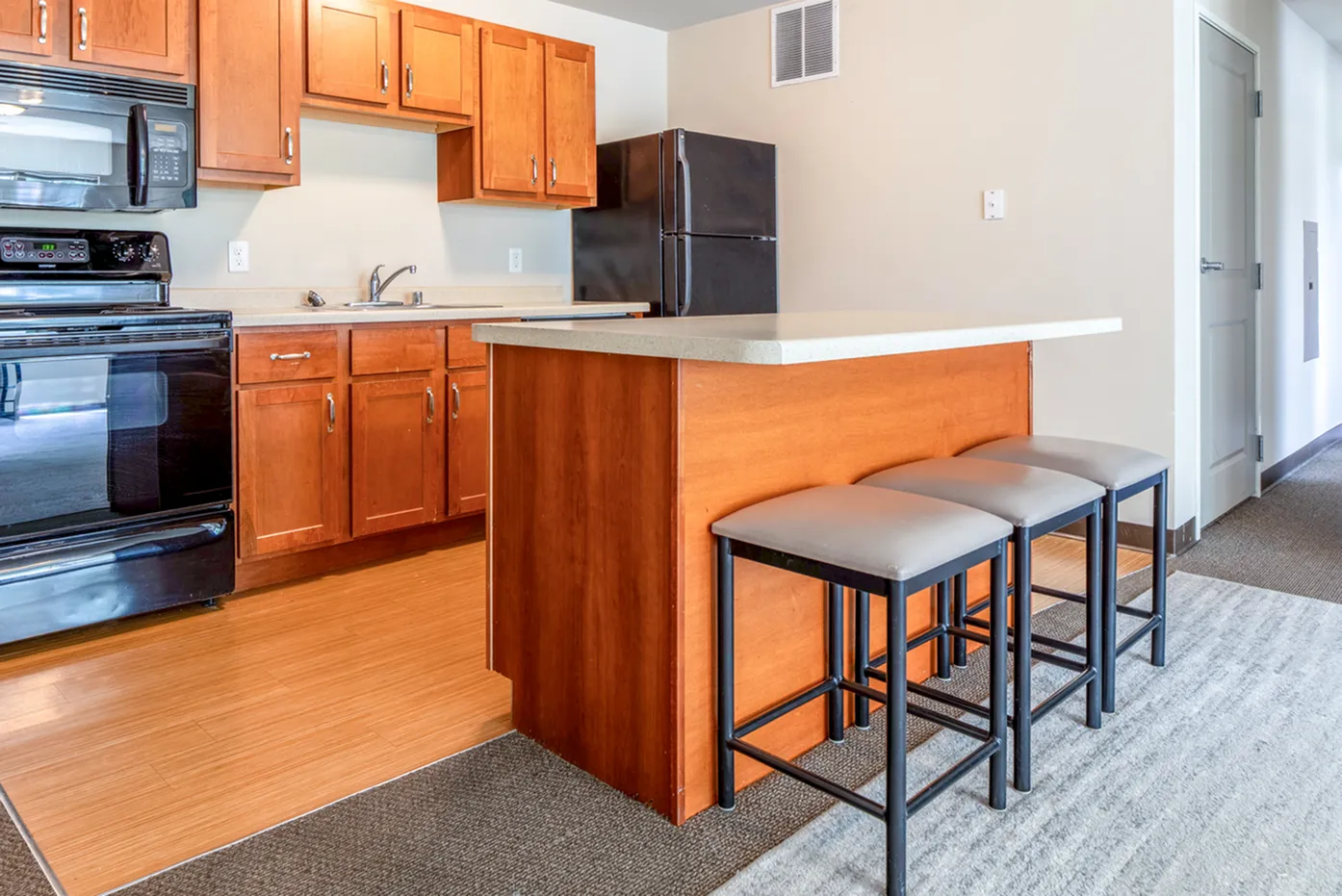 Modern kitchen with wooden cabinets, black appliances, and a cozy island with seating. Bright and inviting space ideal for cooking and dining.