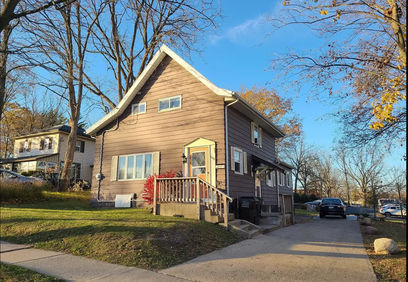 Charming two-story house with a front porch and spacious driveway, surrounded by a peaceful suburban landscape on a sunny day.
