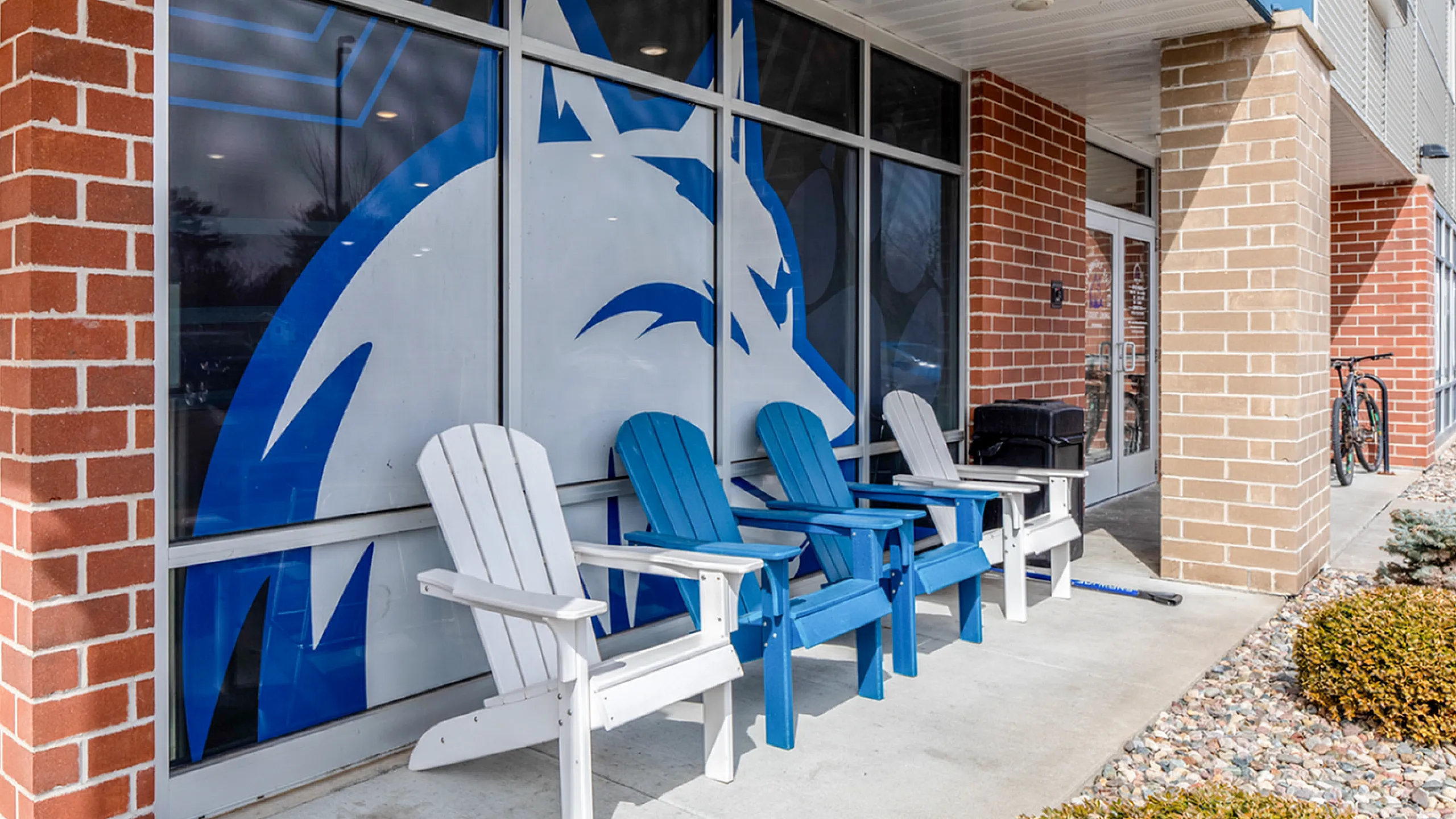 Inviting outdoor seating area with colorful Adirondack chairs against a modern building facade, perfect for relaxation and socializing.