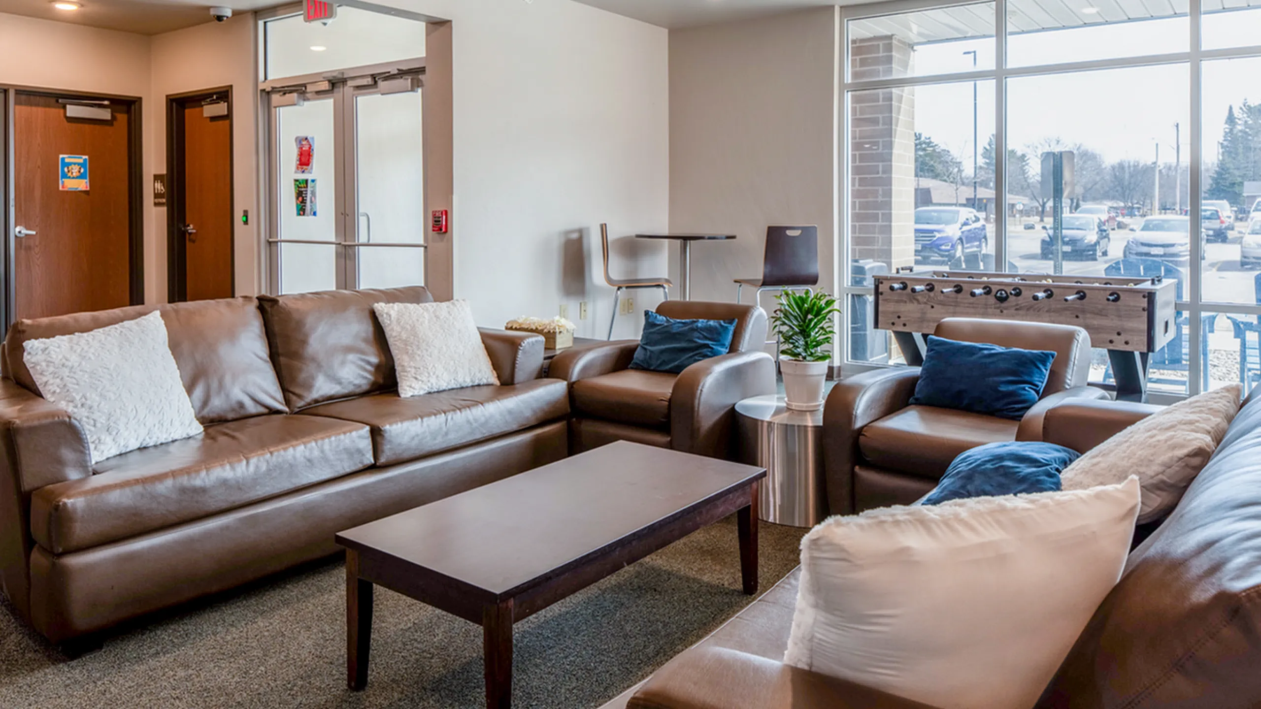 Inviting living room with plush brown leather sofas, elegant foosball table, and large sunlit windows.