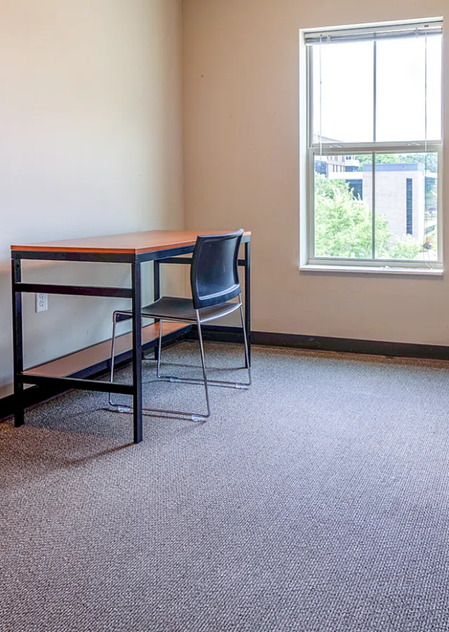 Bright bedroom featuring a large window, sleek desk, and stylish dresser, perfect for productive days and serene views.