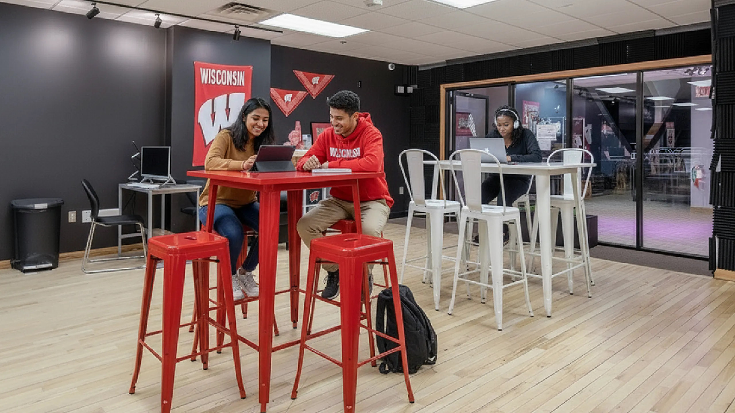 Modern co-working space with vibrant red and white decor, featuring young professionals collaborating at high tables and a cozy atmosphere.