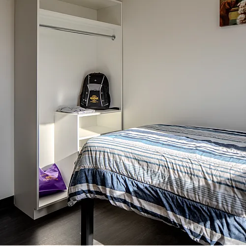 Cozy bedroom with stylish striped bedding and open wardrobe, perfect for modern living.