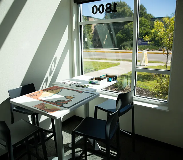 Bright and cozy corner with a modern table and chairs, ideal for leisurely activities, featuring large windows that offer a picturesque view of the greenery outside.