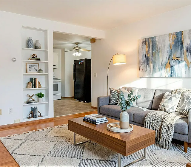 Charming living room with stylish gray sofa, textured cushions, and elegant decor, blending seamlessly into a cozy kitchen with modern appliances.
