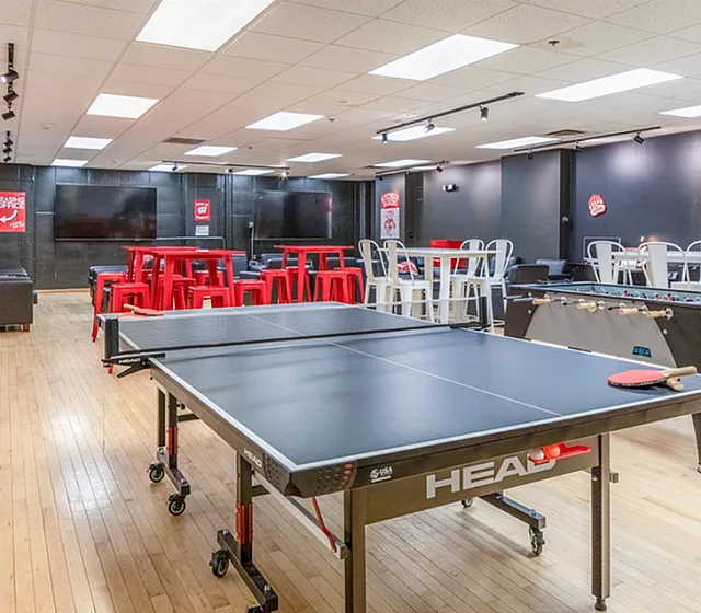 Vibrant recreational room featuring a ping pong table, foosball table, modern seating, and large screens.