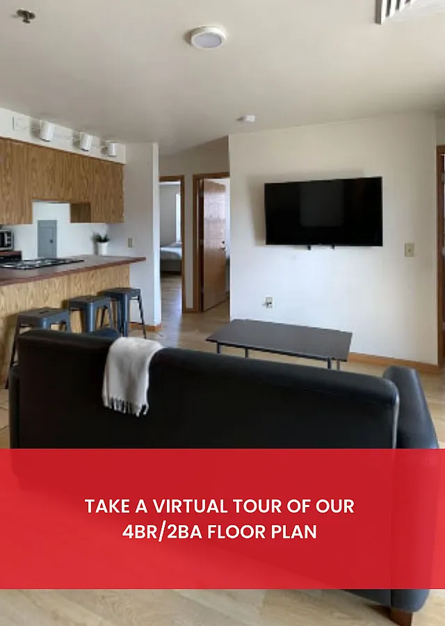 Modern living area with open kitchen, sleek seating, and a wall-mounted TV in a stylish 4BR/2BA apartment. Explore the inviting and functional space.