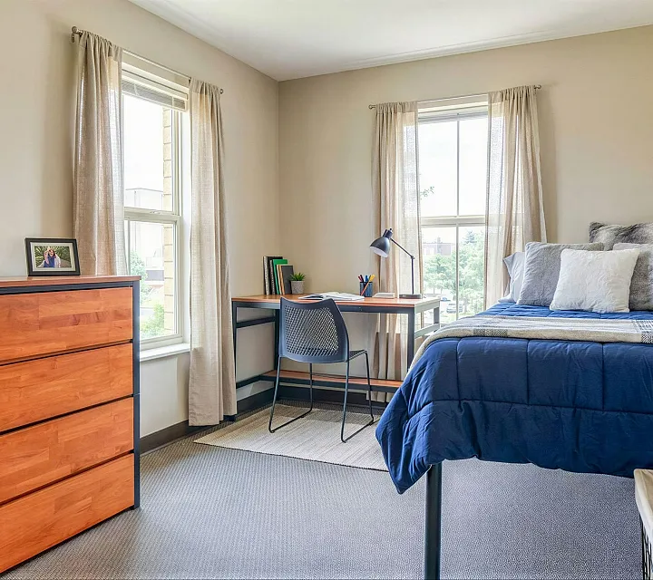 Bright and inviting bedroom showcasing modern decor, cozy bed with plush pillows, elegant desk setup by the window, and stylish wooden dresser.