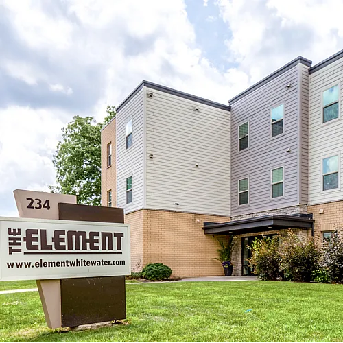 Modern apartment building with sleek design and lush landscaping, featuring 'The Element' sign welcoming residents.