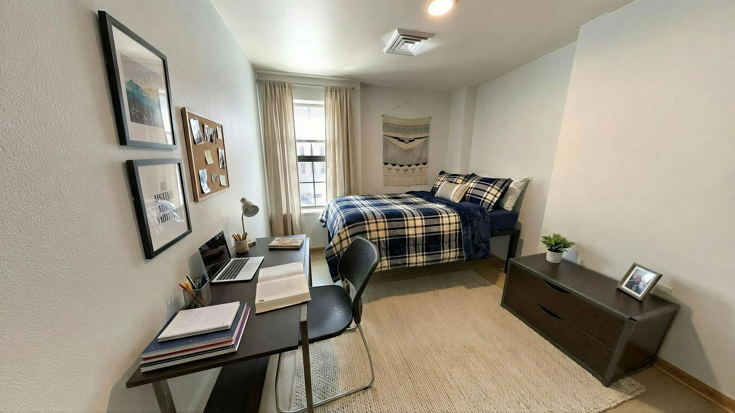 Cozy bedroom with stylish decor featuring a comfortable bed, functional study area with a laptop, and a bright window view.
