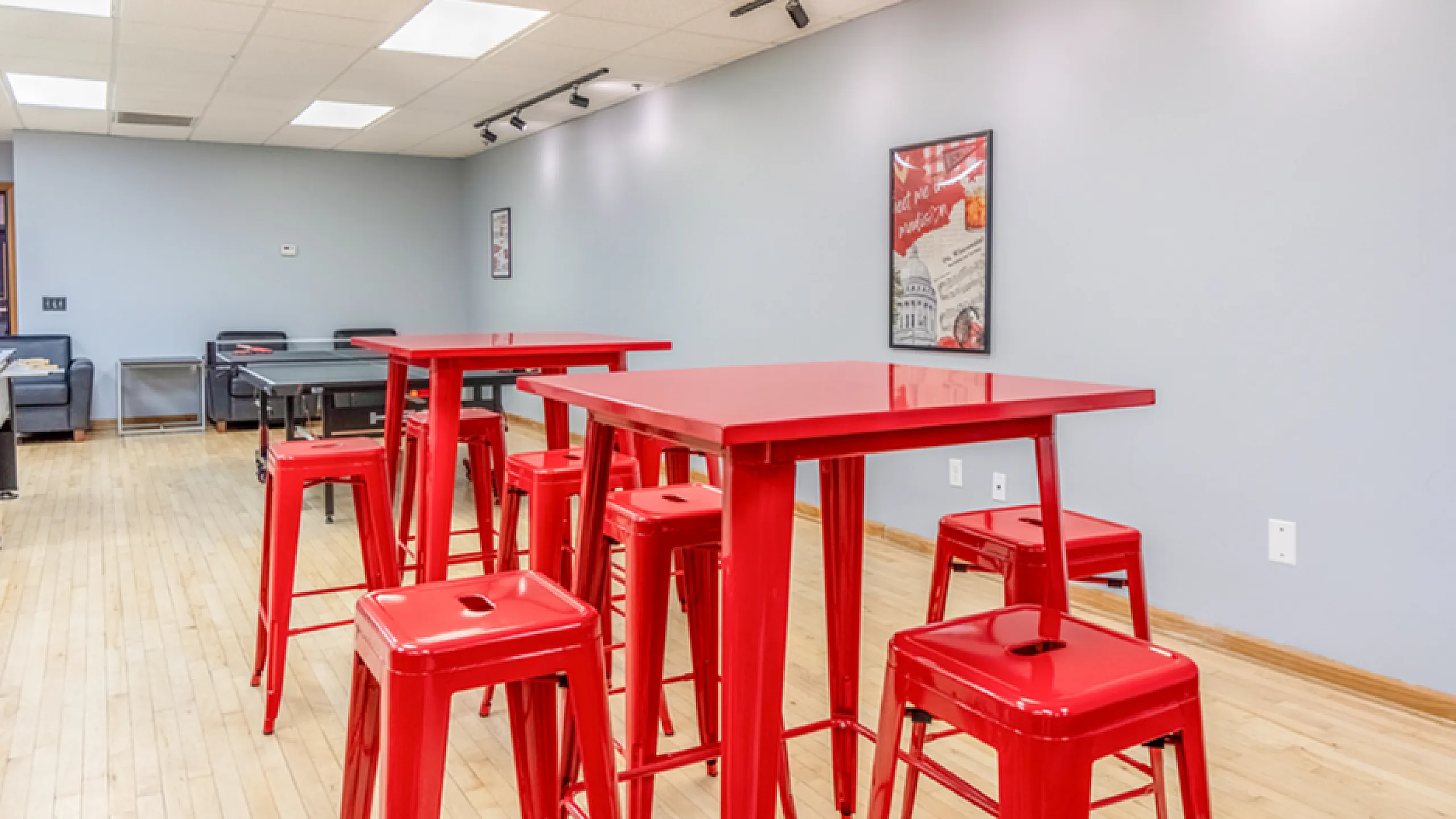 Vibrant community space featuring bright red tables and stools, perfect for social gatherings or casual meetings, highlighted by a sleek wooden floor and modern wall decor.