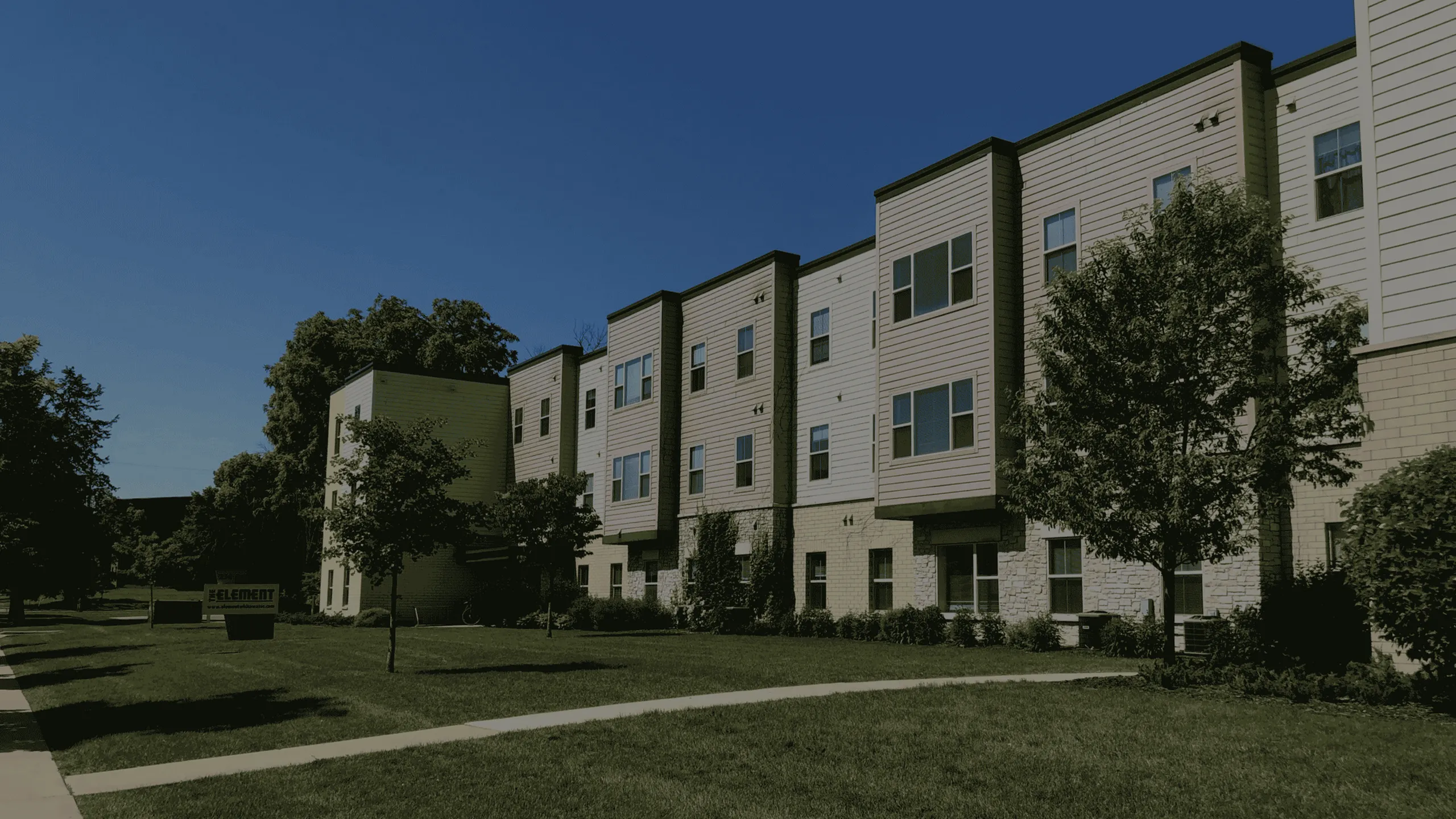 Modern apartment complex with sleek design, surrounded by lush greenery and a clear blue sky.