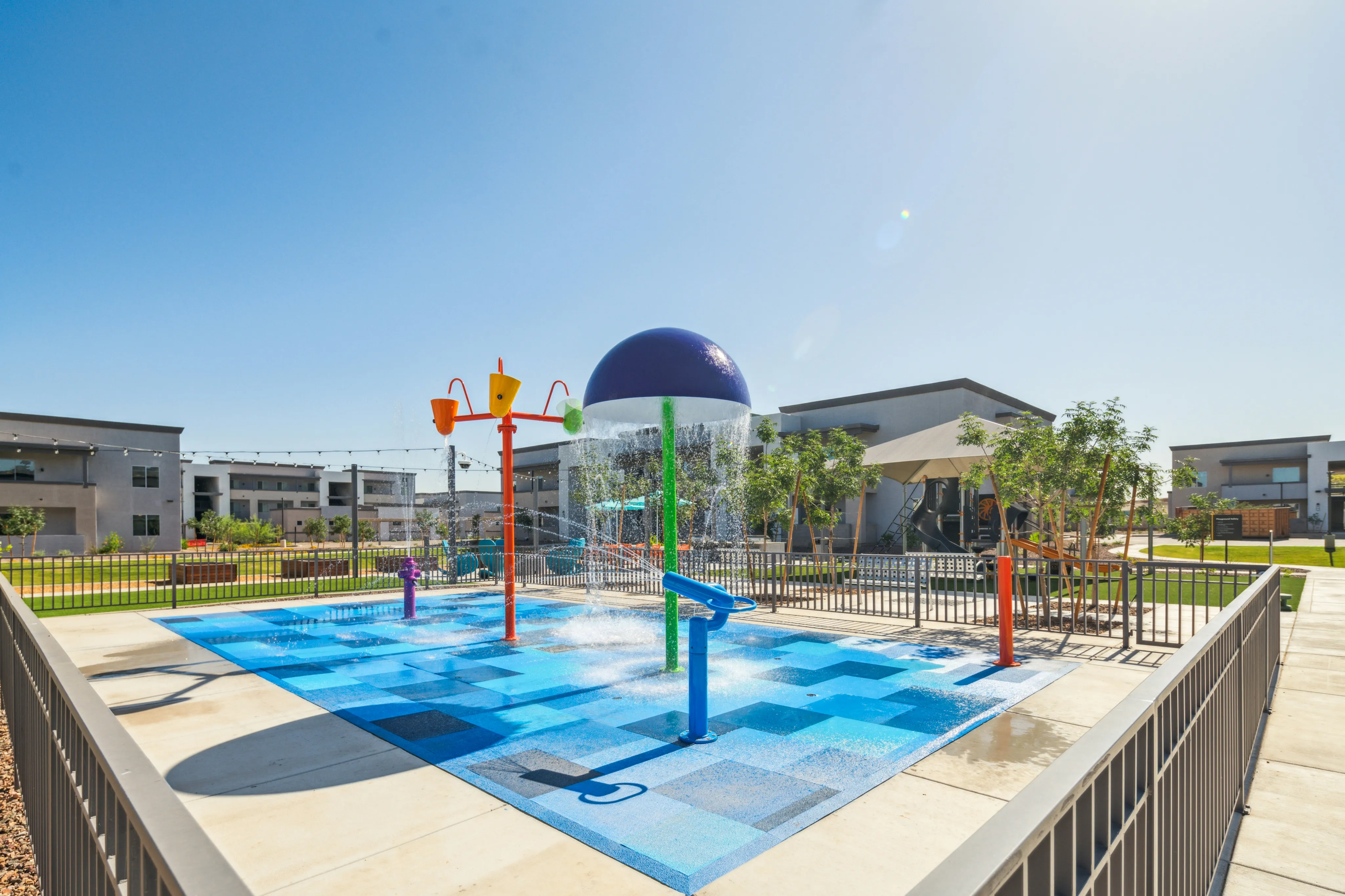 Colorful outdoor splash pad featuring water play equipment and modern apartment buildings in the background.
