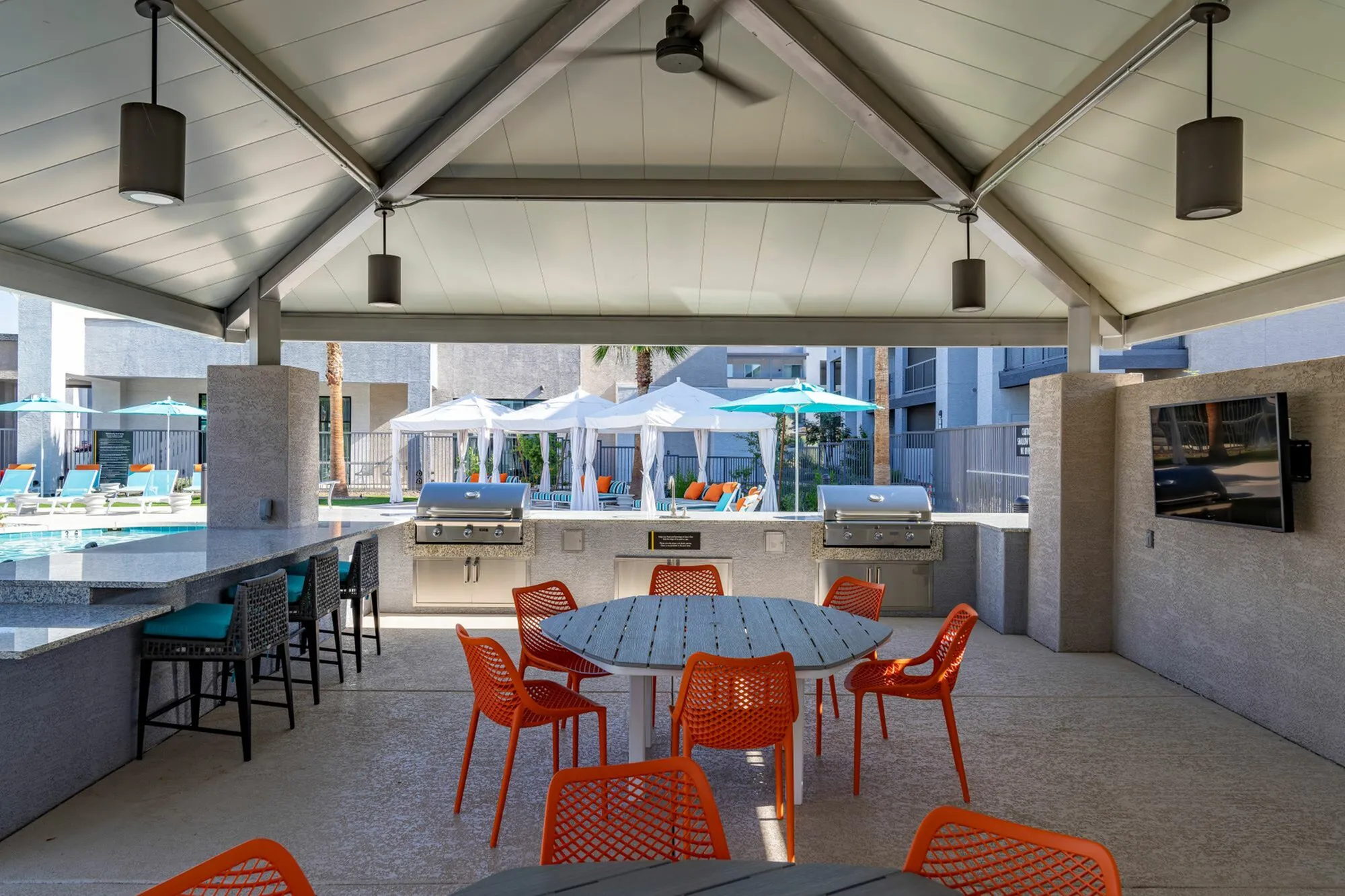 Modern outdoor lounge with vibrant orange seating, shaded grilling area, and inviting poolside cabanas under a stylish pavilion.
