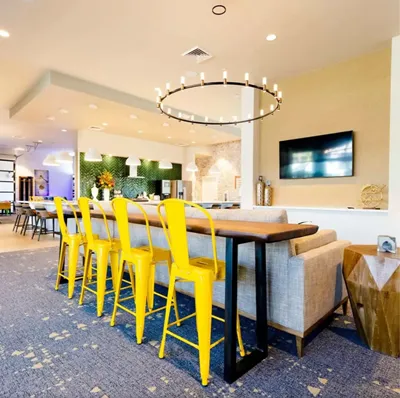 Chic open-concept apartment with vibrant yellow bar stools, modern lighting, and a stylish living area perfect for entertaining.