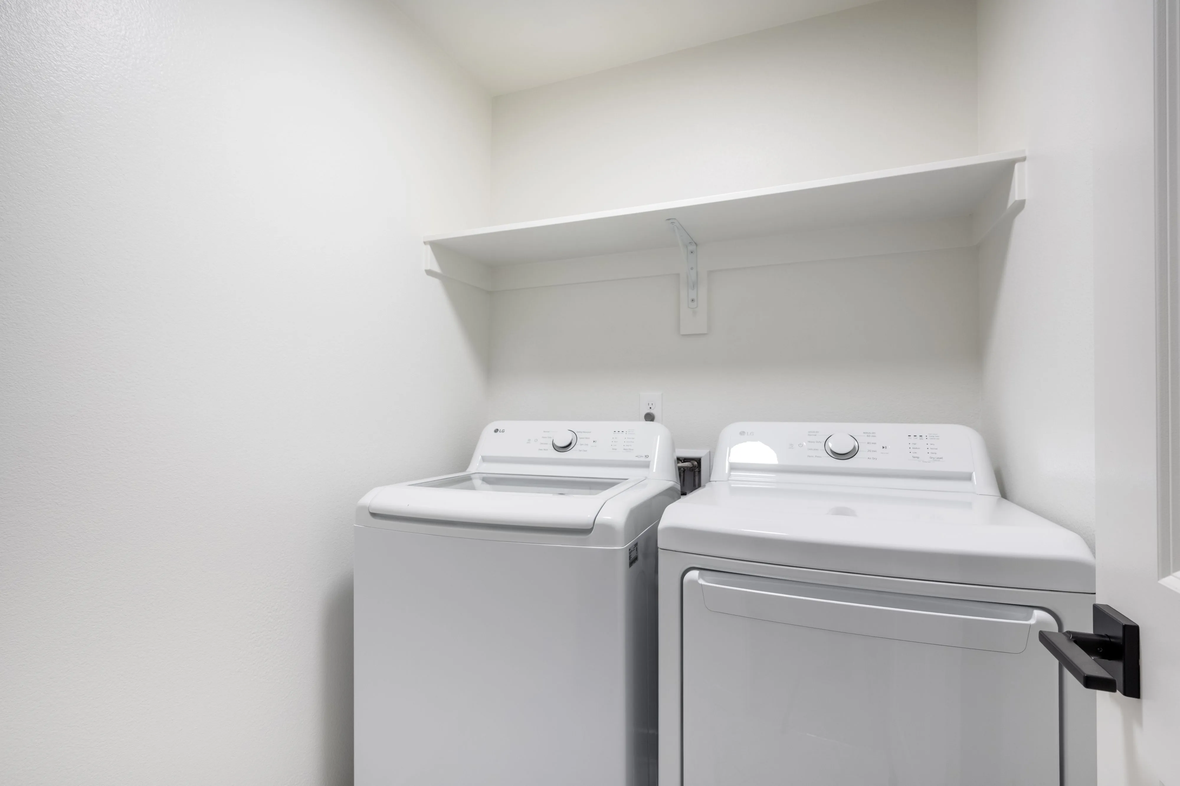 Modern laundry room with sleek white washer and dryer set beneath a convenient storage shelf.