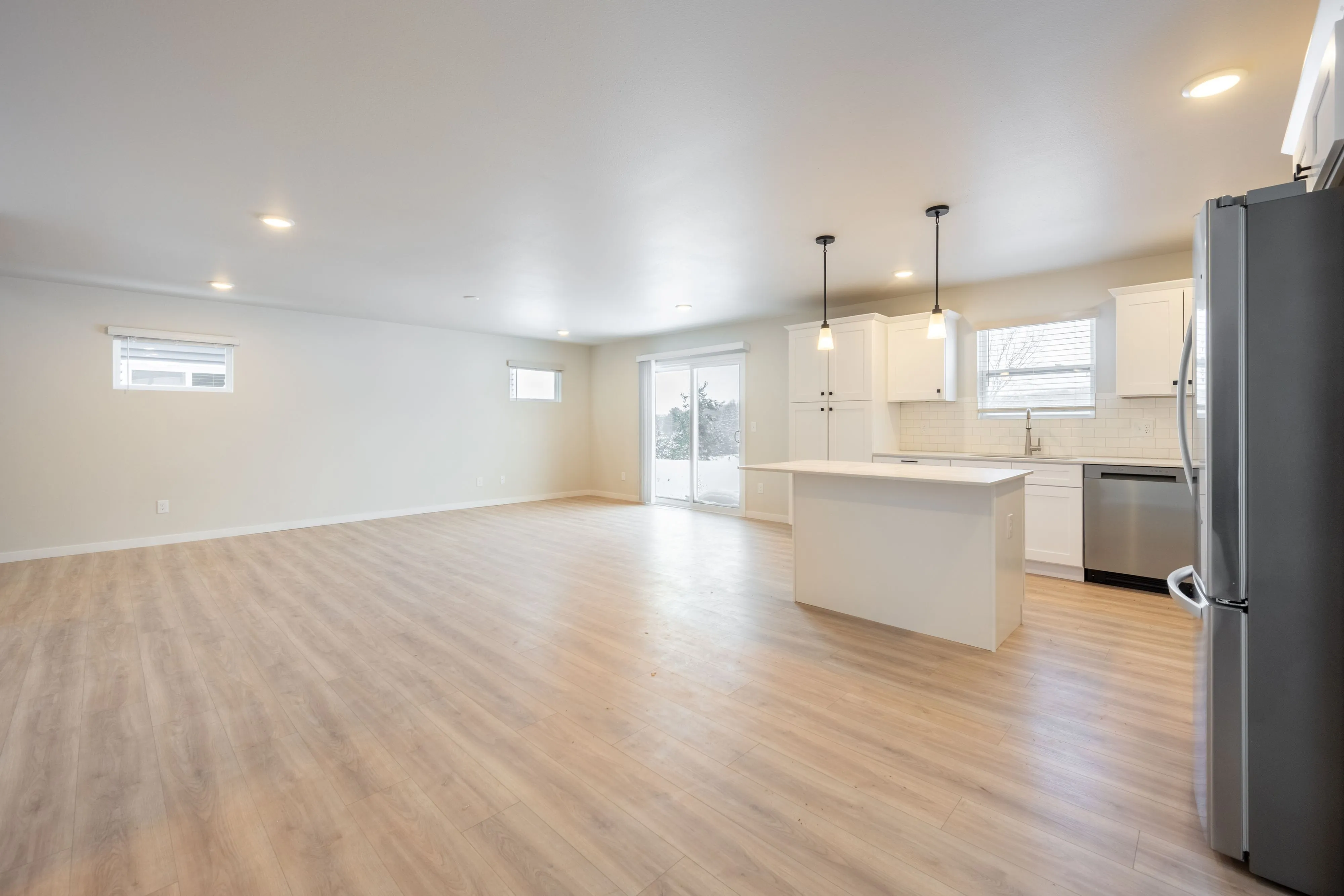 Bright and airy open-plan living space with sleek kitchen island, modern appliances, and elegant plank flooring flooring.
