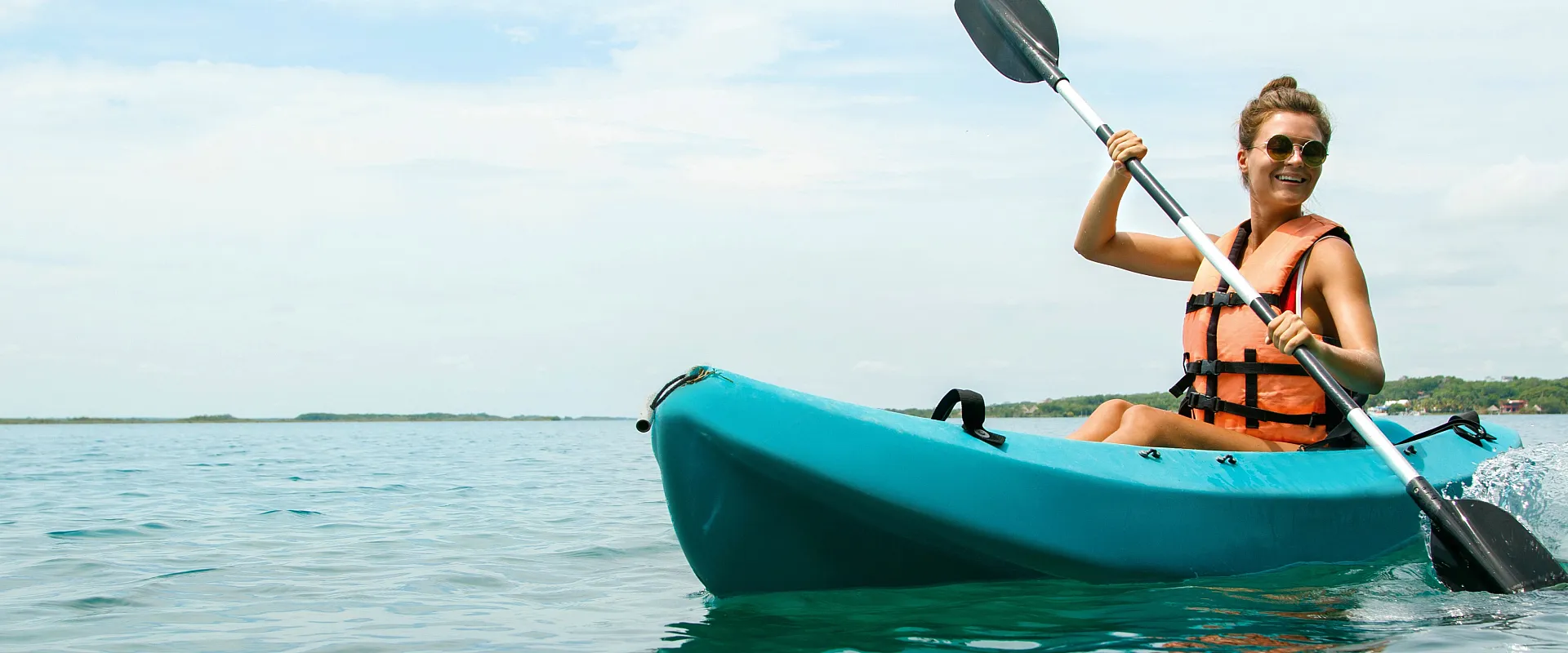 Joyful woman kayaking in a serene turquoise ocean under a bright blue sky, epitomizing adventure and relaxation.