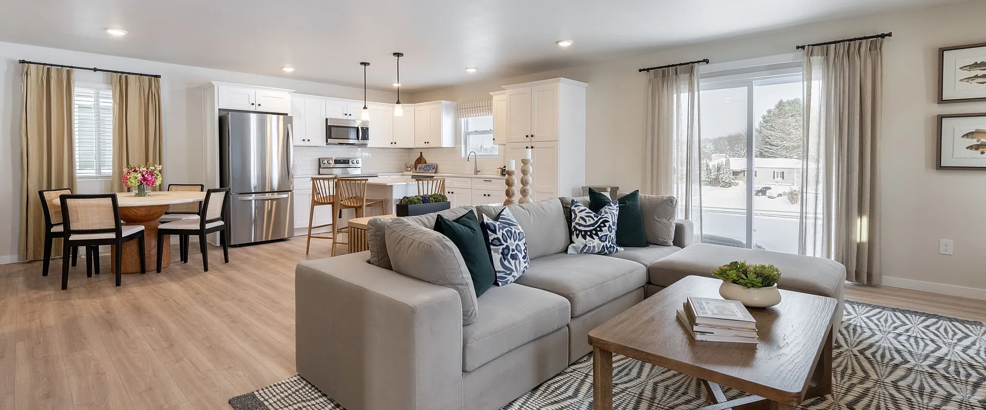 Bright open-plan living area showcasing a comfortable gray sofa, stylish dining nook, and modern kitchen with stainless steel appliances.
