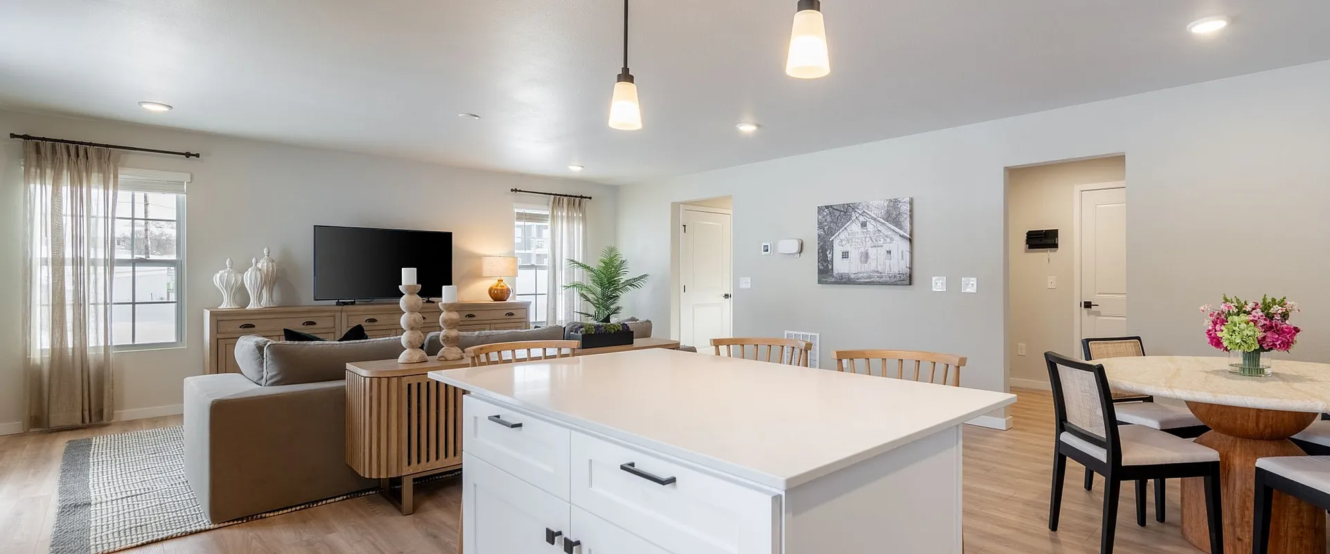 Bright, modern open-concept living space featuring a sleek kitchen island, cozy seating area, and elegant dining table with fresh flowers.