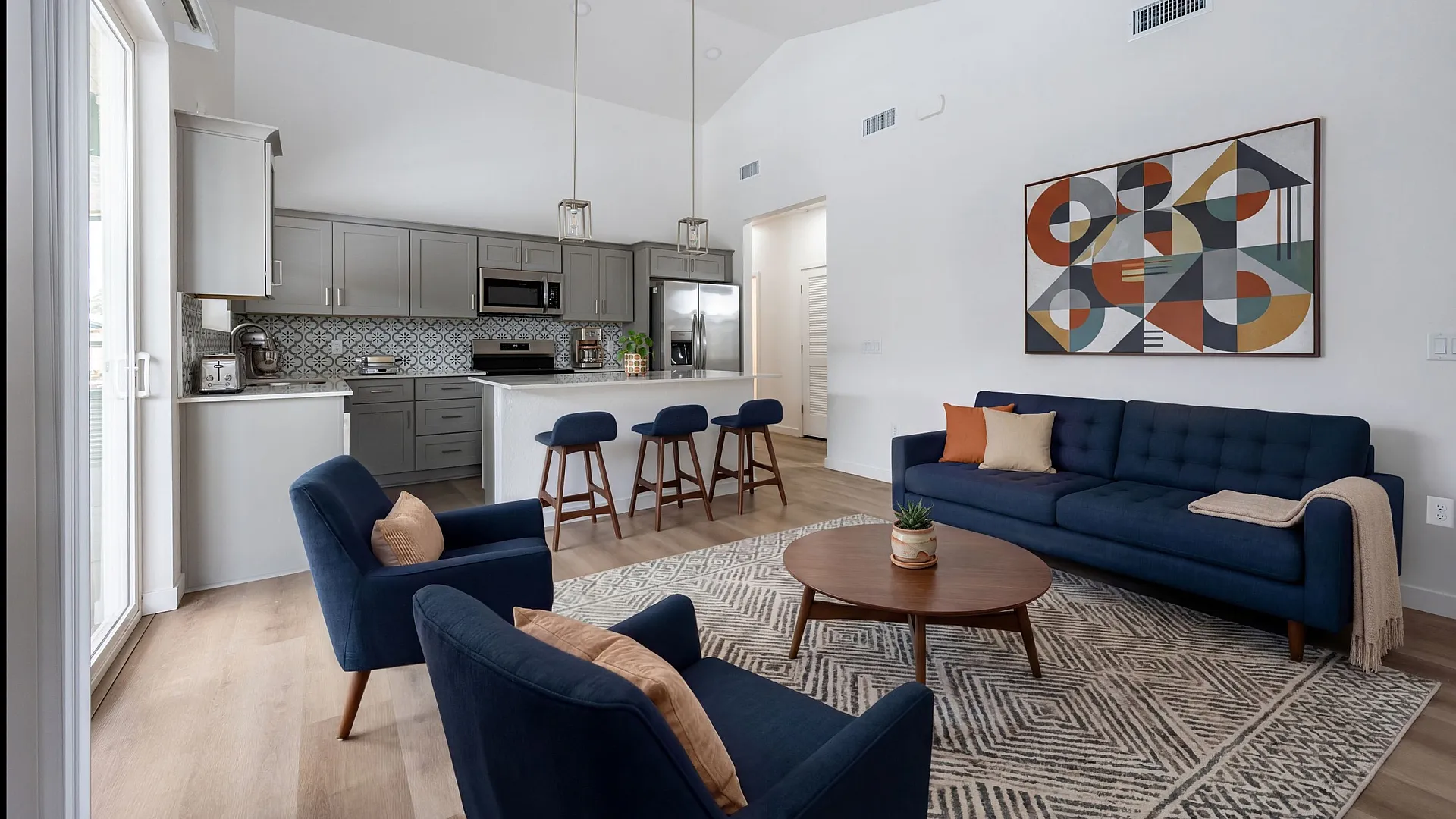 Elegant open-plan living room and kitchen with modern decor, featuring stylish blue furniture and chic geometric artwork.