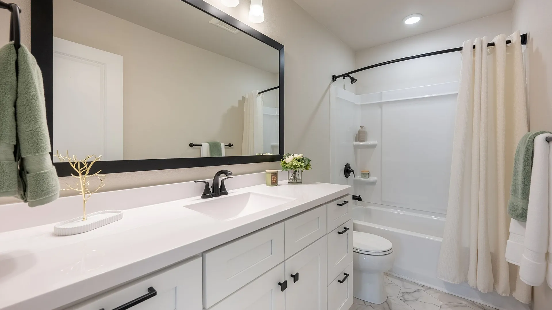 Elegant bathroom design featuring a sleek white vanity with black accents, large mirror, and cozy tub area.