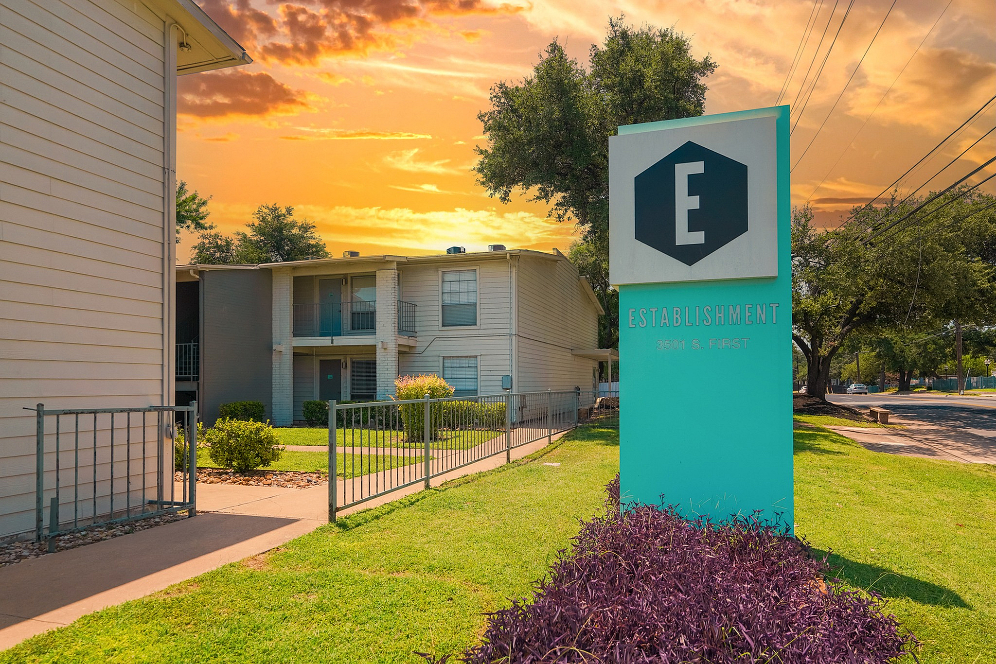 Charming apartment complex with vibrant exterior, lush landscaping, and a stunning sunset backdrop at Establishment Apartments.