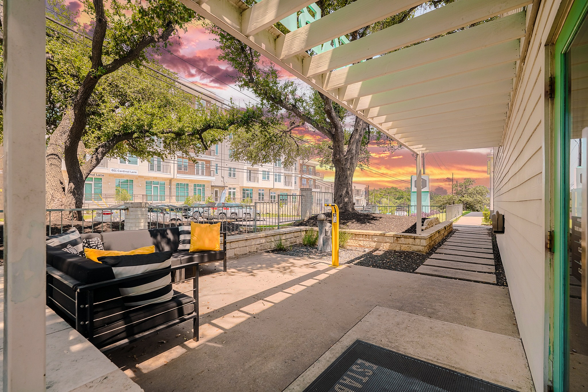 Inviting outdoor seating area with modern furniture under a pergola, set against a stunning sunset sky and lush trees.