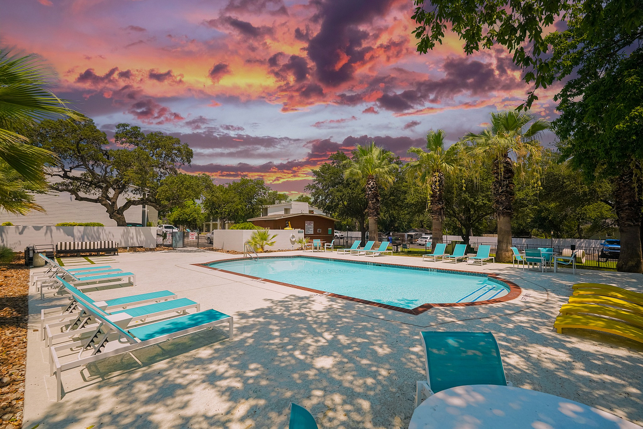 Inviting pool area with modern loungers and lush greenery under a stunning sunset sky.