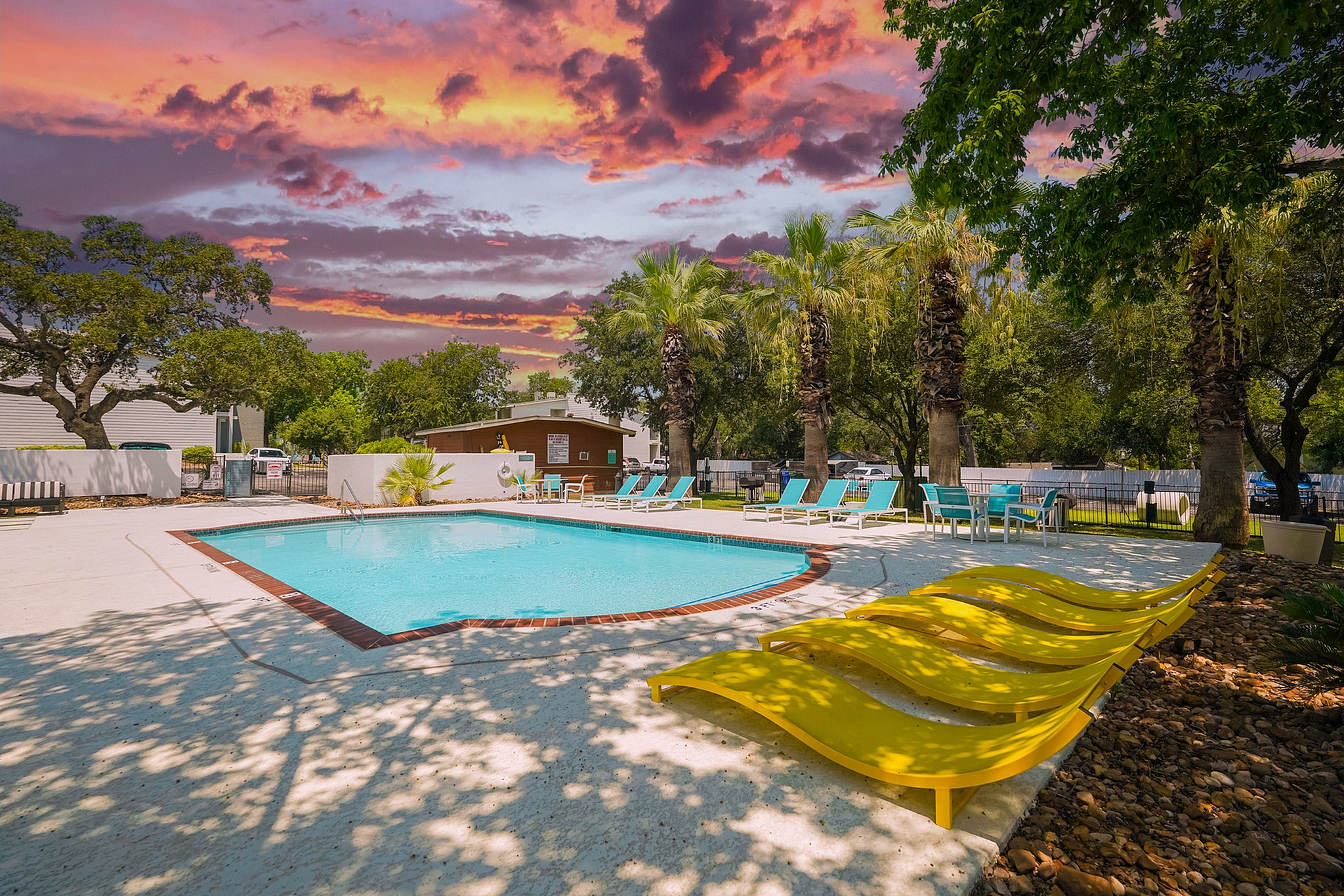 Stunning pool area with vibrant yellow loungers and palm trees, set against a dramatic sunset sky, creates a tropical paradise.