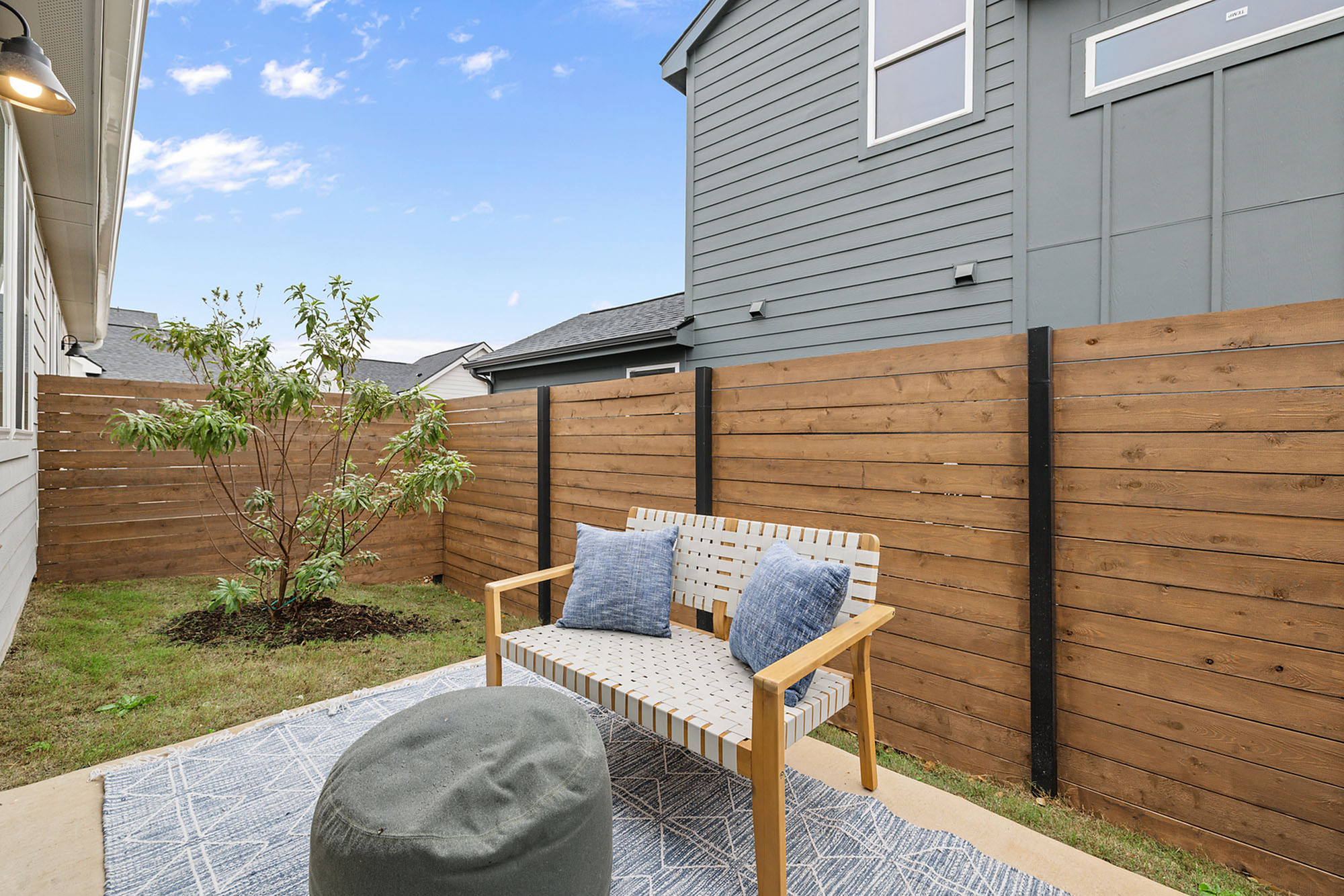 Charming outdoor nook with cozy seating and cushions, enclosed by a modern wooden fence and greenery.
