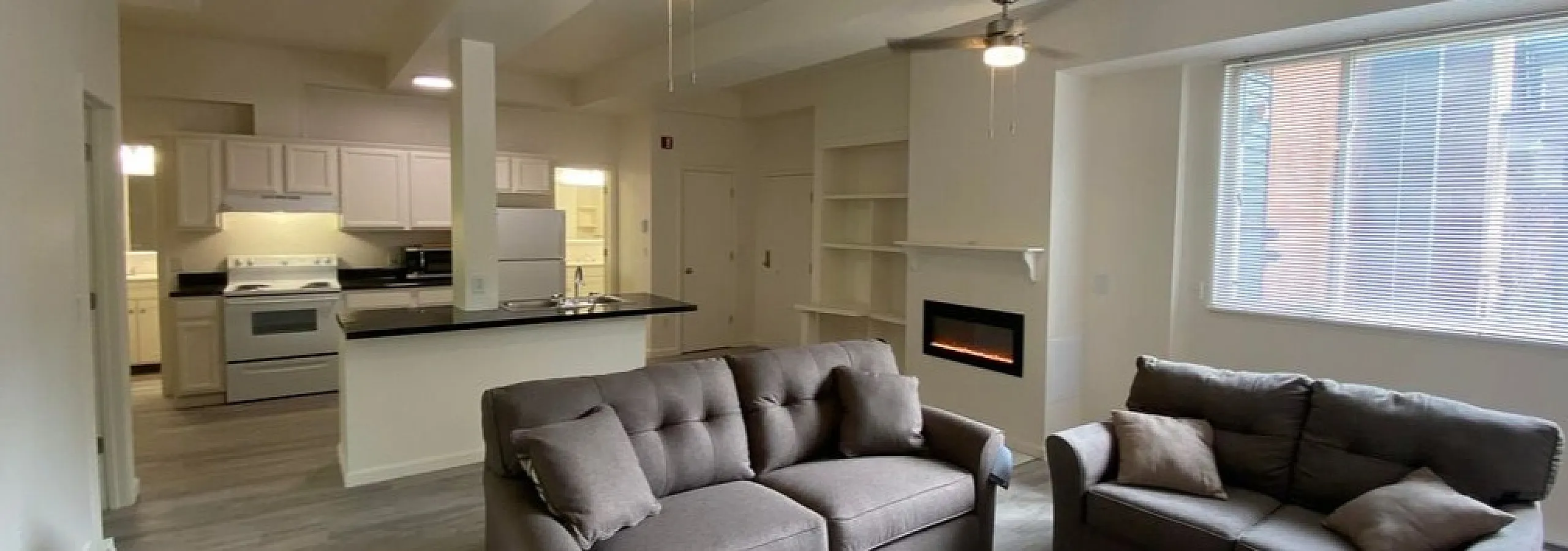 Modern open-concept living room with cozy sofas, elegant fireplace, and a bright kitchen in the background.