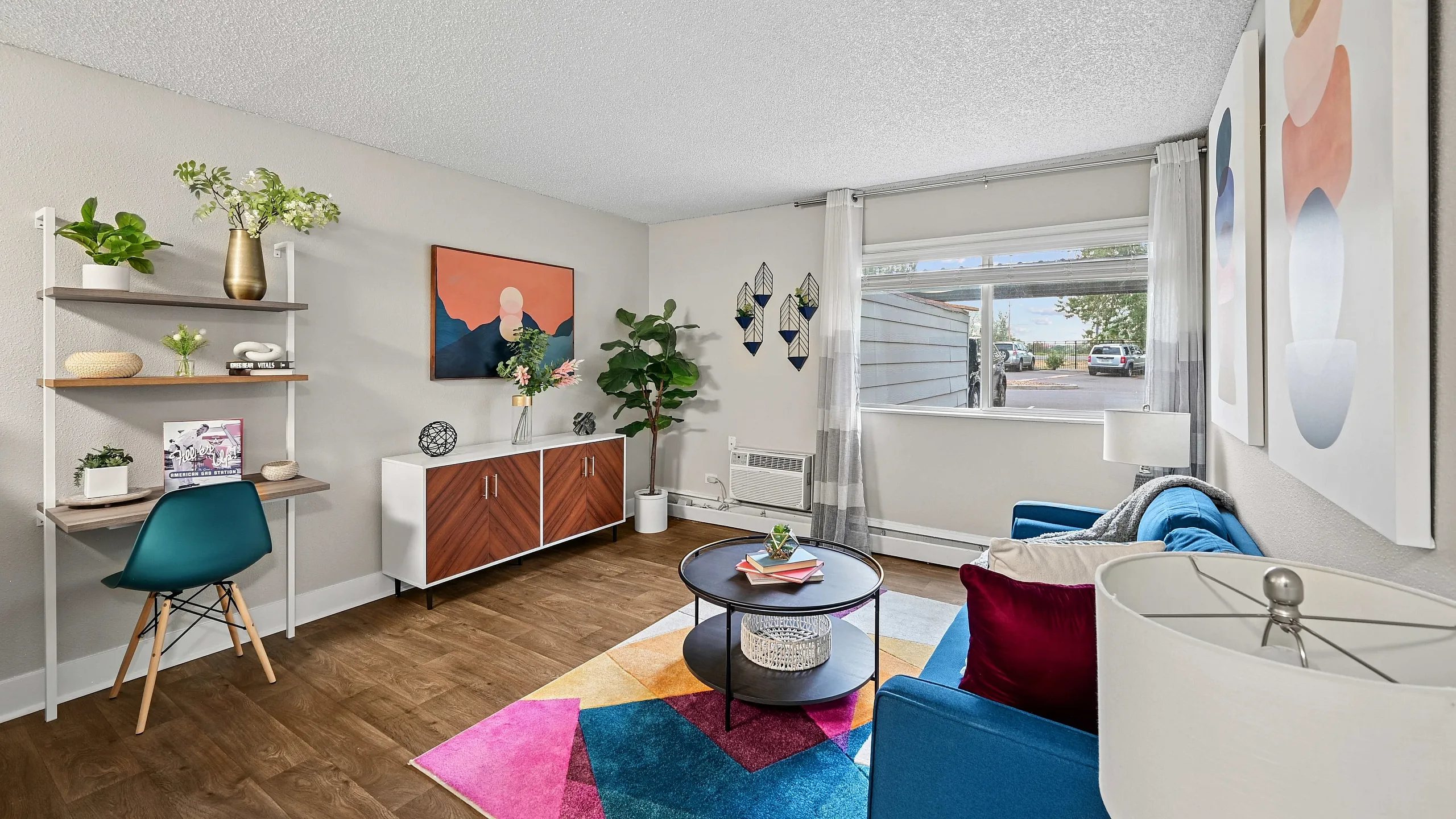 Charming apartment living room with modern furnishings, vibrant d&eacute;cor, stylish artwork, and natural light through a large window.