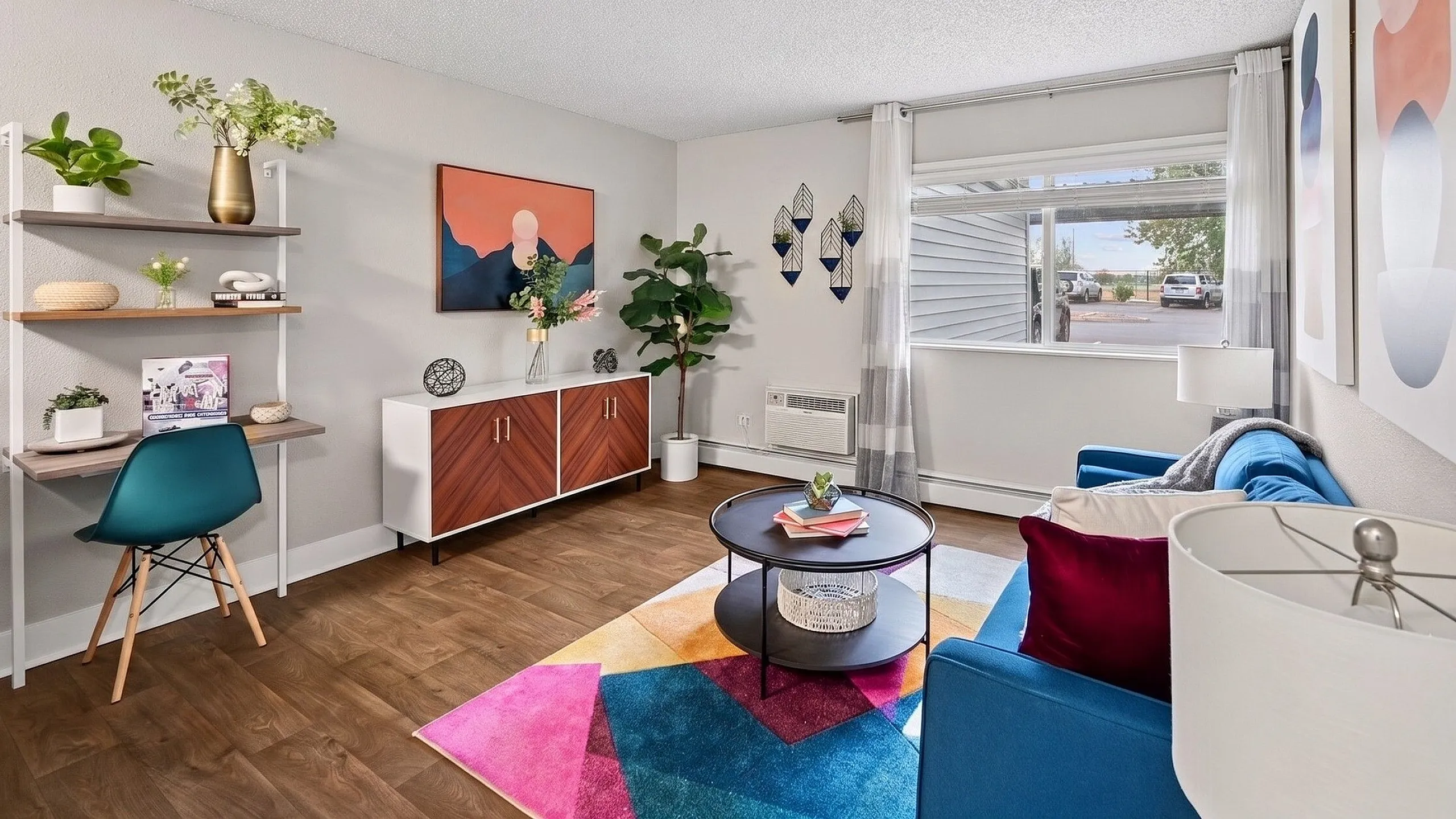 Bright and inviting apartment living room with stylish decor, featuring a modern desk, vibrant artwork, and large window for natural light.
