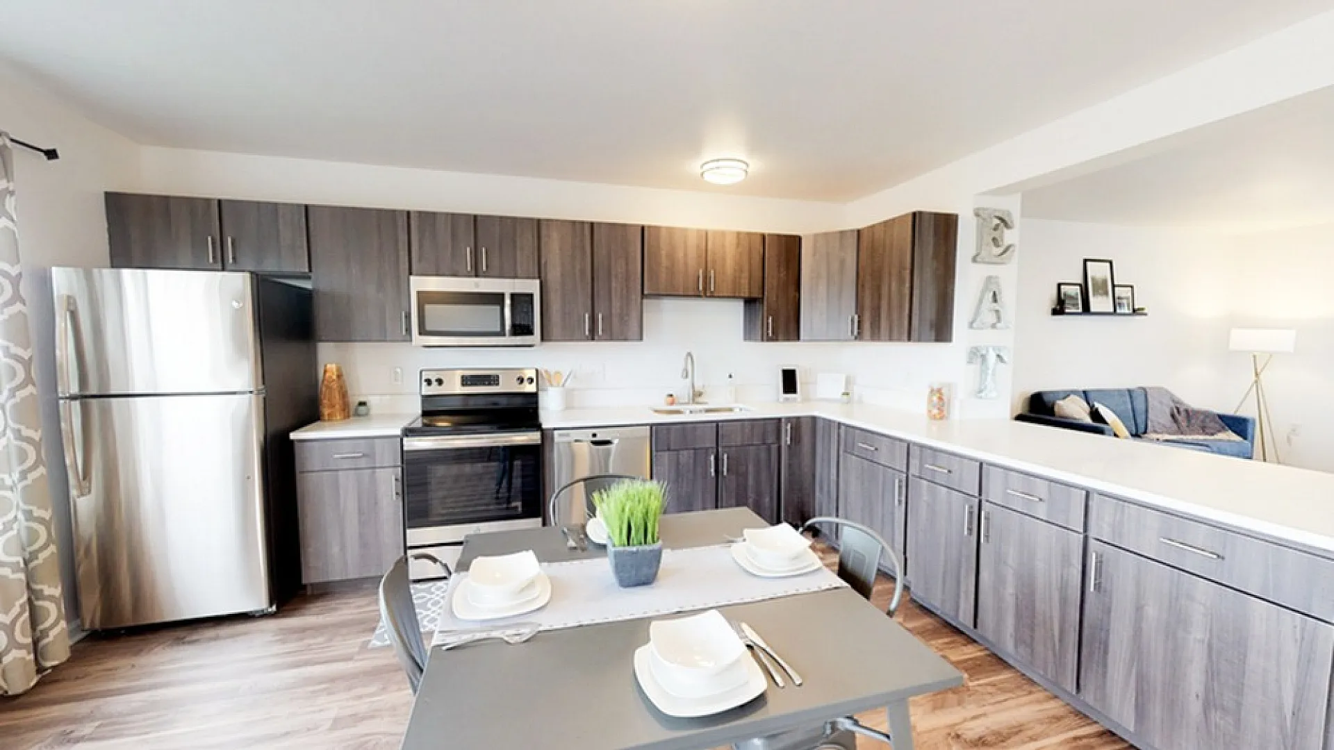 Modern kitchen with sleek stainless steel appliances, stylish gray cabinets, and a cozy dining nook leading into a bright, inviting living area.