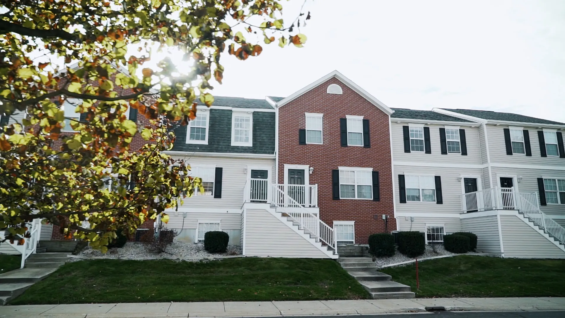 Charming townhouse exterior with classic brick and siding, surrounded by lush greenery and a welcoming entryway.