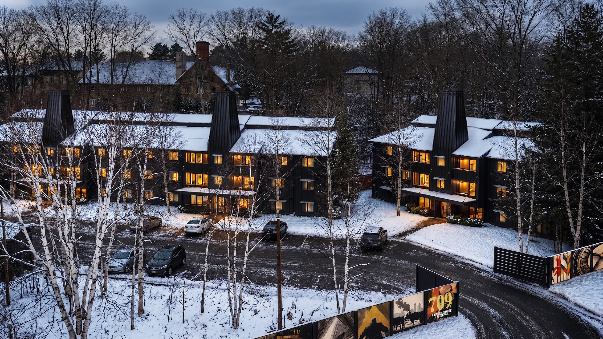 Charming snow-covered apartment complex nestled in a serene woodland setting with warm glowing windows.